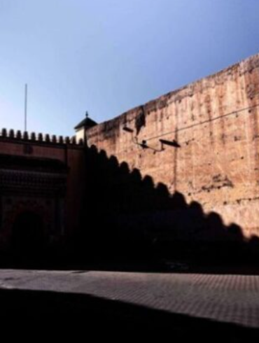 Cinematic photo of a person walking past a massive city wall in Morocco, a scene perfect for Moroccan photo tours.