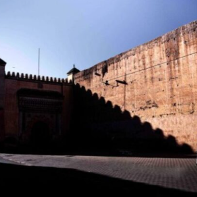 Cinematic photo of a person walking past a massive city wall in Morocco, a scene perfect for Moroccan photo tours.