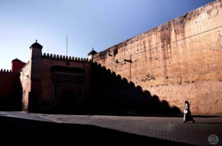 Cinematic photo of a person walking past a massive city wall in Morocco, a scene perfect for Moroccan photo tours.