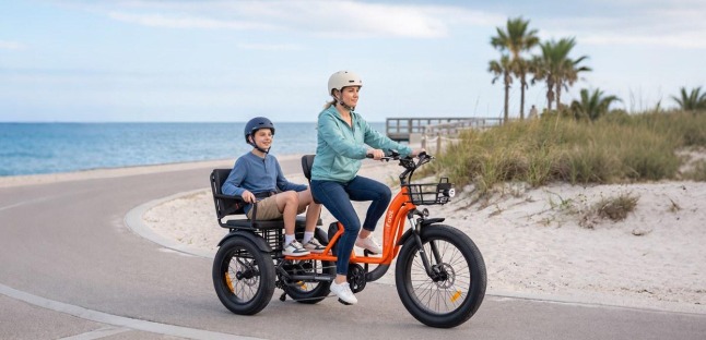 Adult and young passenger riding an orange electric trike with passenger seat on a coastal road